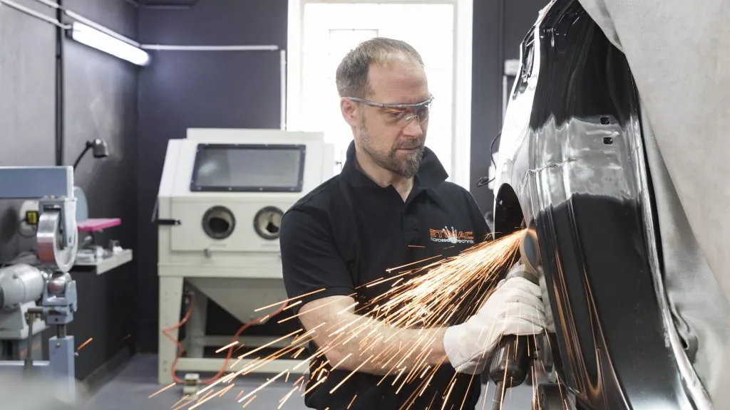 Karosseriebauer von STIMAC trennt mit der Flex ein Karosserieteil, Funken sprühen in der Werkstatt