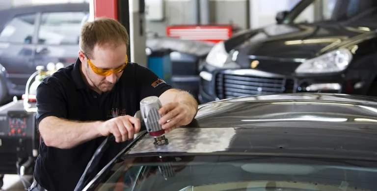 Mitarbeiter bearbeitet die Lackfläche eines Fahrzeugdachs mit einem Smart-Repair-Gerät